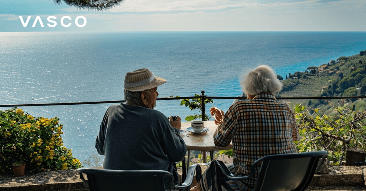 Una coppia anziana beve il caffè su un balcone con vista mare.