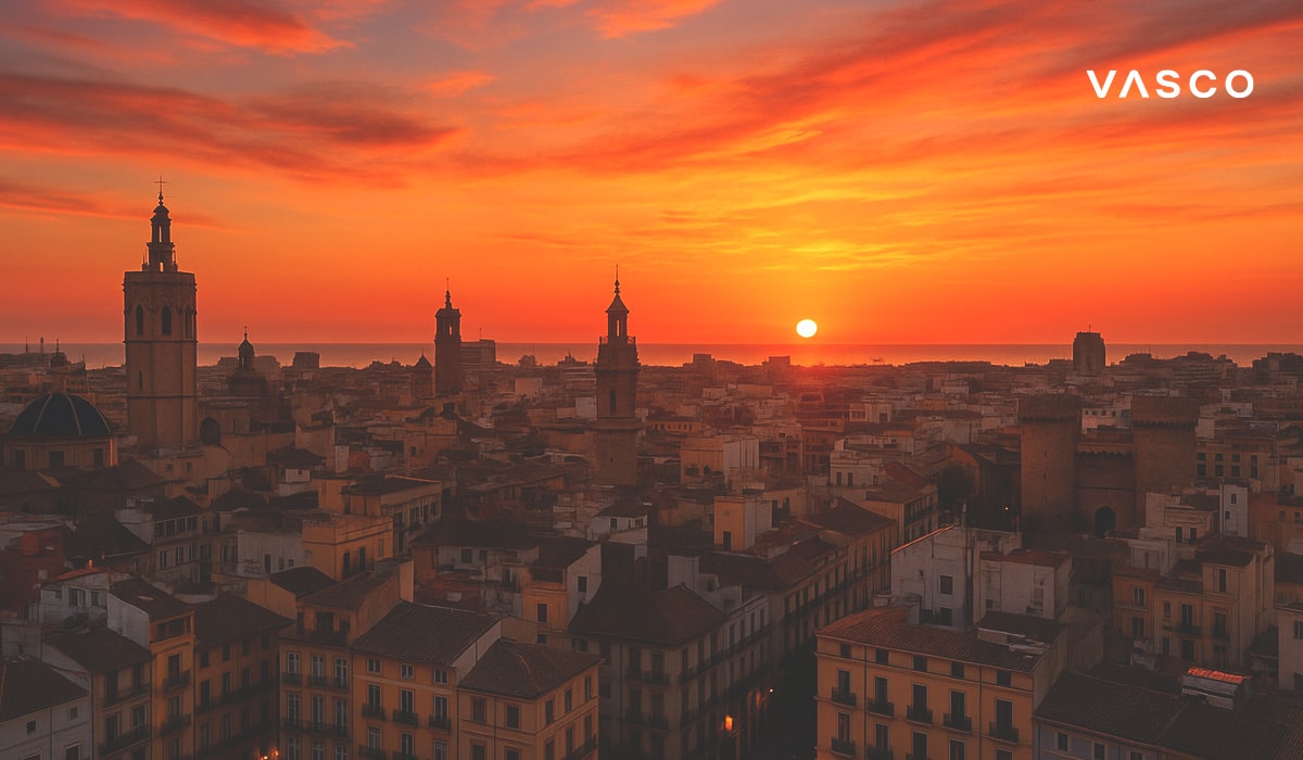 Veduta aerea di Valencia, Spagna, all’alba, con torri storiche e tetti sotto un drammatico cielo arancione.