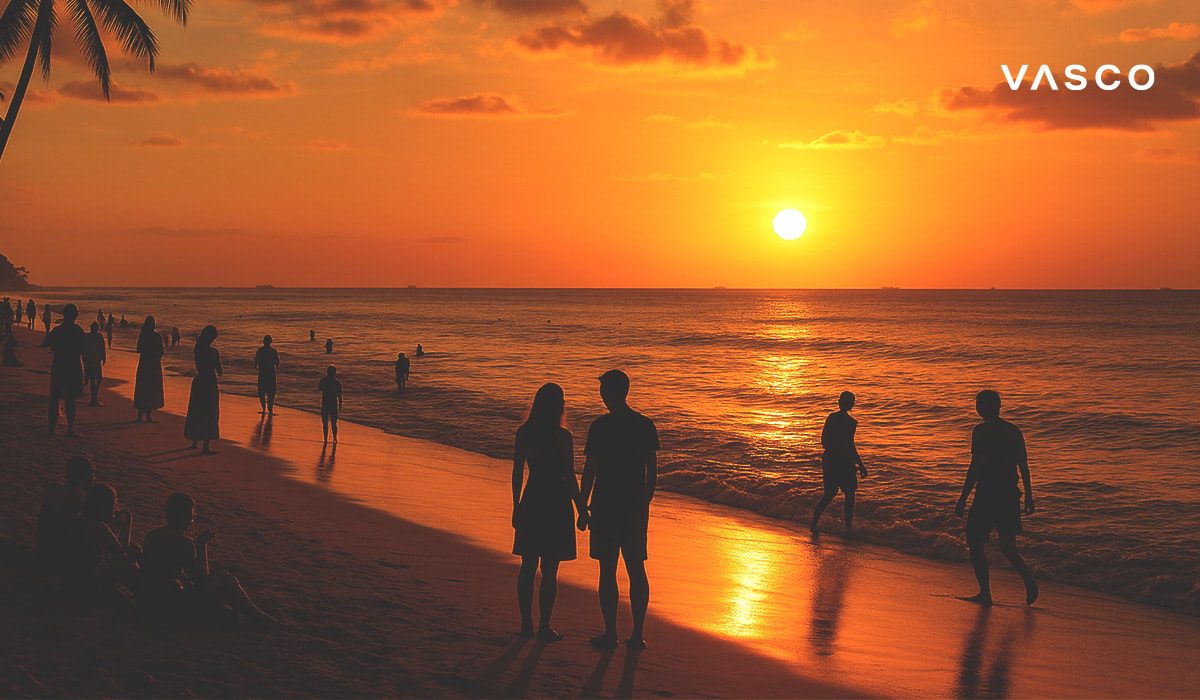 Una coppia che guarda un bellissimo tramonto arancione su una spiaggia di Bali, con altre persone intorno.