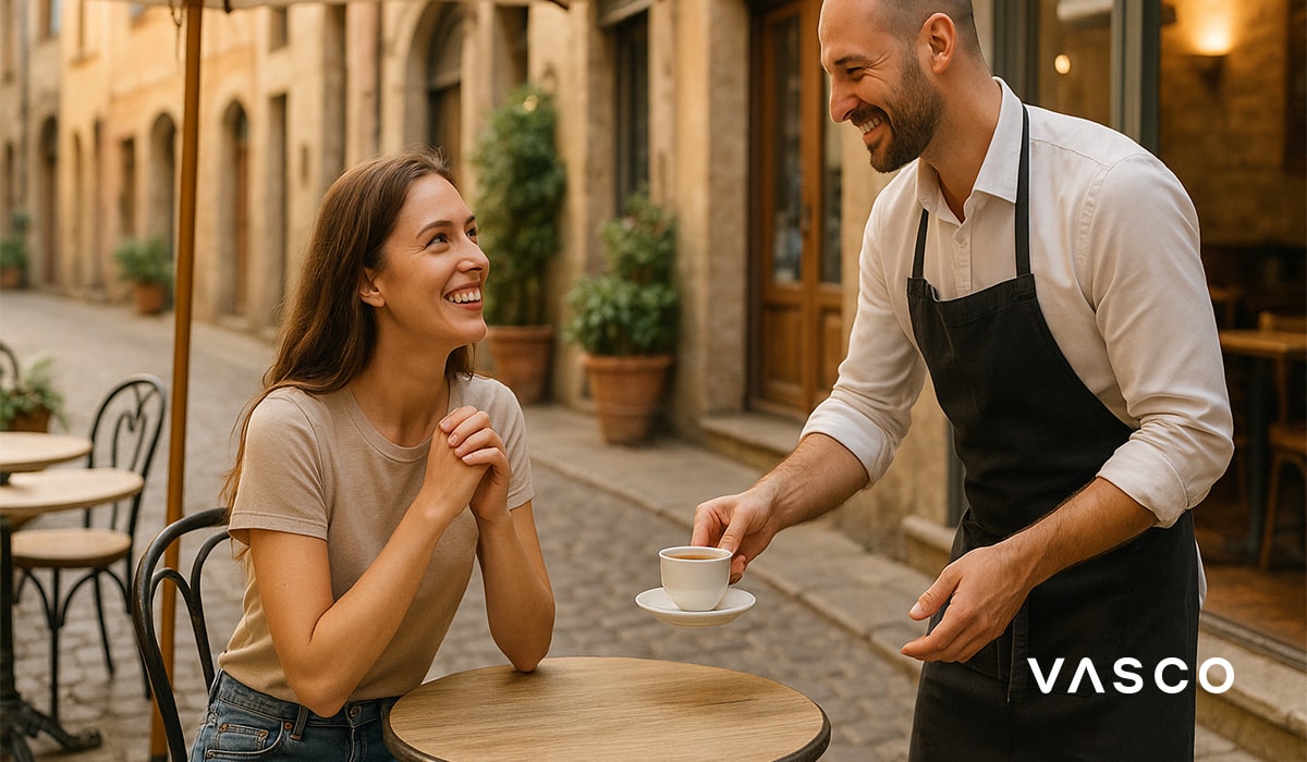 Cameriere che serve il caffè a una donna seduta a un tavolino di un caffè all’aperto