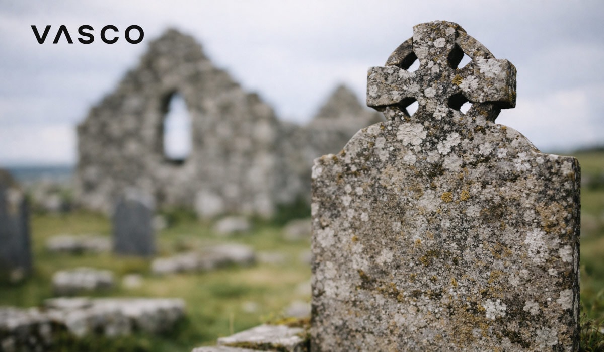 Lapide con croce celtica consumata dal tempo vicino ad antiche rovine in pietra.