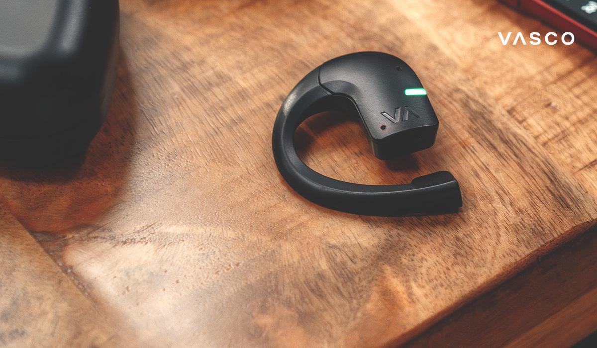 Auricolare Vasco Translator E1 in primo piano su un tavolo di legno con indicatore LED.