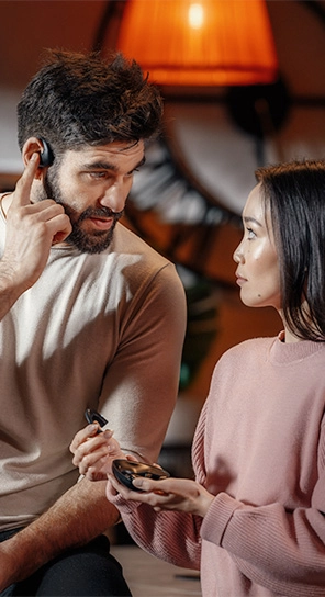Un uomo che indossa un auricolare Vasco Translator E1, in piedi accanto a una donna che tiene in mano il dispositivo E1, ne mette in evidenza i potenti altoparlanti e il microfono intelligente.