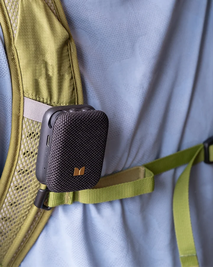 Mini altoparlante Bluetooth nero agganciato al cinturino verde oliva di uno zaino