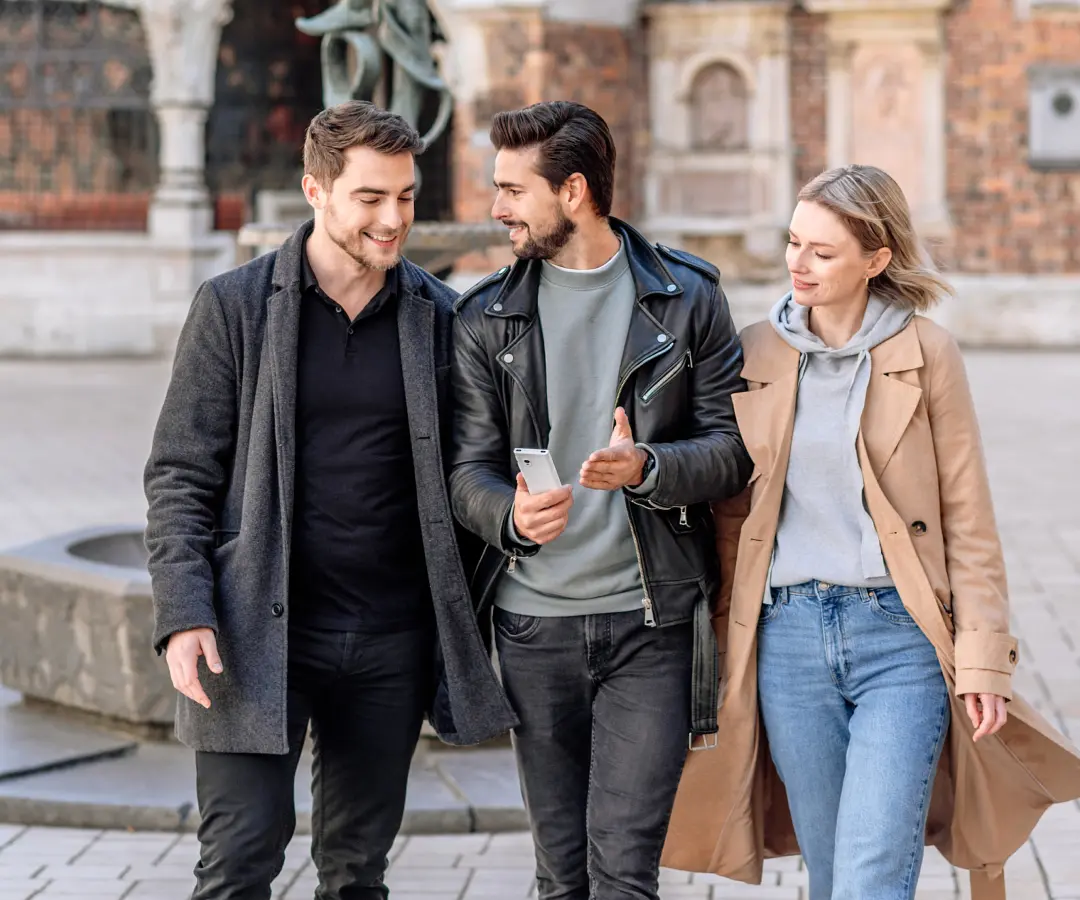 Un uomo tiene in mano un traduttore ed è circondato da amici. Sullo sfondo è visibile l'architettura storica